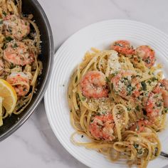 pasta with shrimp and parmesan cheese in a skillet next to lemon wedges