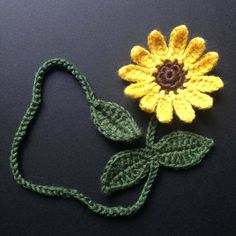 a crocheted yellow flower with green leaves on a black surface next to a string