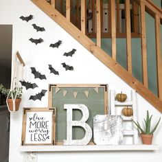 halloween decorations are displayed on the mantle in front of a stair case, with bats flying overhead