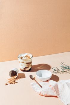 a bowl of cereal next to a cup of yogurt and a spoon on a table