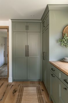 a kitchen with green cabinets and wood flooring next to a wooden counter top in front of a white wall