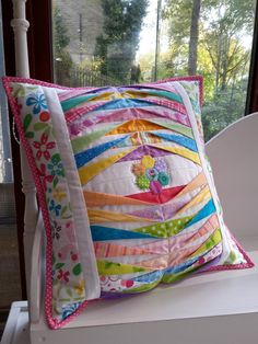 a colorful pillow sitting on top of a white chair next to a window sill