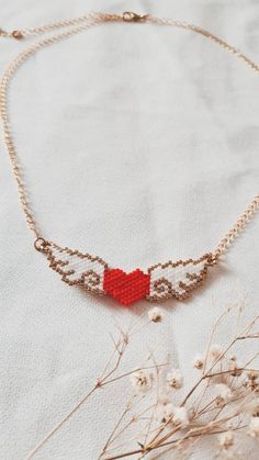 a red beaded heart is hanging from a gold chain on a white cloth background