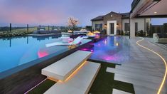 an outdoor swimming pool with benches next to it and lights on the water at night