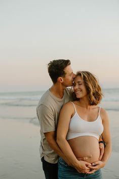 a pregnant couple cuddles on the beach at sunset