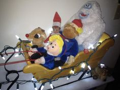 several stuffed animals in a sleigh with christmas lights on the floor behind them