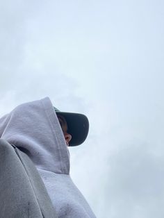 a man wearing a hoodie looking up into the sky with clouds in the background