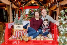 a man and woman sitting in the back of a red truck with christmas decorations on it