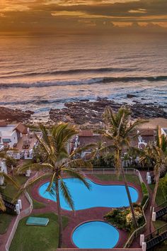 an aerial view of the pool and beach at sunset or sunrise, with palm trees in foreground