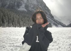 a woman standing in the snow with her hands on her face and mountains behind her