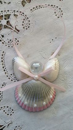 a seashell with a pink ribbon tied around it sitting on a doily covered table