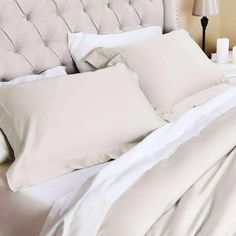 a bed with white sheets and pillows on top of it next to a night stand