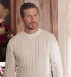 a man in a white sweater standing next to flowers