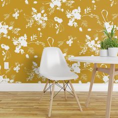 two white chairs and a table in front of a yellow wall with flowers on it