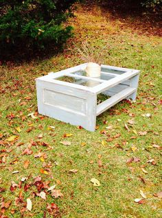 a white coffee table sitting on top of a grass covered field next to bushes and trees