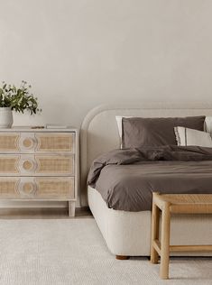 a white bed sitting next to a wooden dresser with a plant on top of it