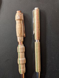 two pens sitting next to each other on top of a black surface and one has a wooden figure