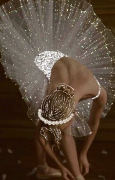 a woman in a white dress is bending down with her hand on the ground and holding a fan