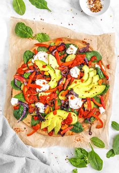 an uncooked pizza with tomatoes, avocado and spinach on top