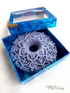 a blue box with an intricately designed object in the inside, sitting on a white surface