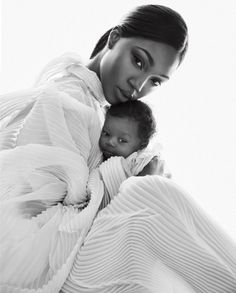 a woman is holding a baby wrapped in a white blanket and posing for the camera