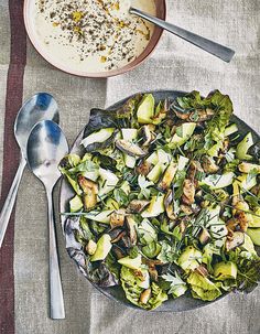 a bowl of soup and a plate of salad on a tablecloth with spoons