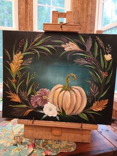 an easel with a painted pumpkin and flowers on it