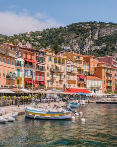 several boats are docked in the water next to some buildings and umbrellas with mountains in the background