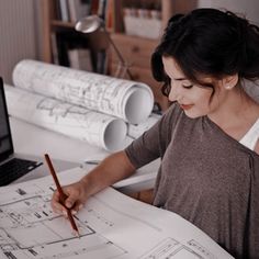 a woman sitting at a desk working on blueprints