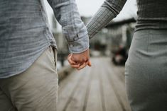 two people holding hands while walking on a boardwalk