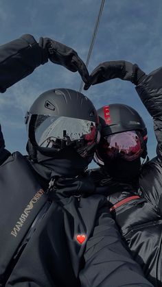 two people in black jackets and helmets holding their hands together