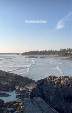 the beach is surrounded by large rocks and water with trees in the backgroud