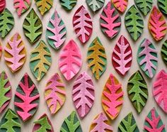 some very pretty colorful paper leaves on a white wall with pink, green and yellow colors