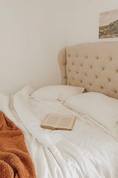 an open book sitting on top of a bed with white sheets and pillows in a bedroom