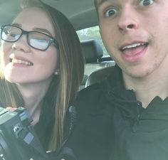 a man and woman sitting in the back seat of a car, taking a selfie