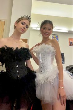 two beautiful young women standing next to each other wearing dresses with feathers on the skirt