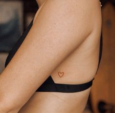 a woman with a small heart tattoo on her left side chest and arm, wearing a black bra