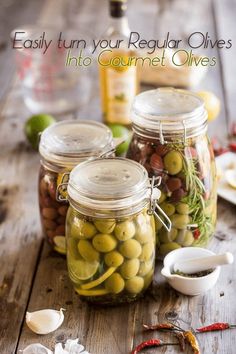 three jars filled with olives sitting on top of a wooden table next to spices