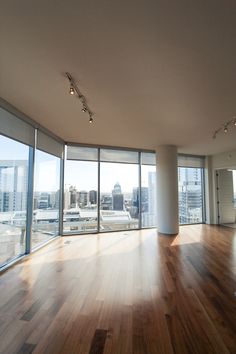 an empty room with wooden floors and large windows looking out on the cityscape