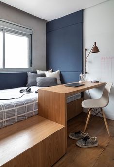 a bed sitting next to a desk in a bedroom under a window with blue walls