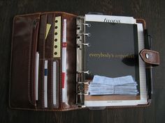 an open leather planner book on a wooden table with pens, pencils and other office supplies