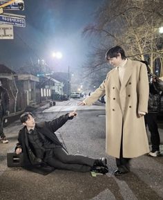 a man in a trench coat pointing at another man laying on the ground with his hand out