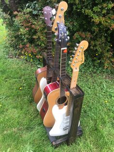 three guitars are stacked on top of each other in front of some bushes and flowers