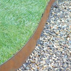 a bird is sitting on the edge of a garden bed with gravel and grass around it