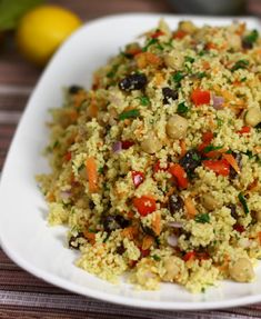 a white bowl filled with rice and vegetables on top of a table next to lemons