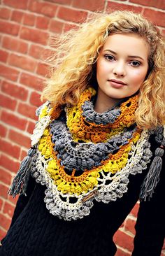 a woman standing in front of a brick wall wearing a yellow and gray crocheted scarf