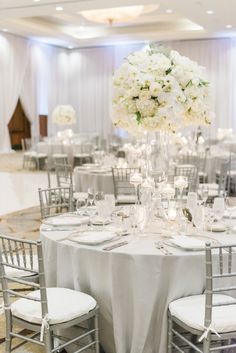 the tables are set with white flowers and silver chairs