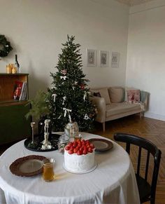 a small christmas tree in the corner of a living room next to a table with fruit on it