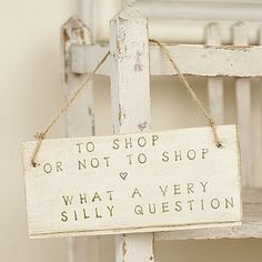 a wooden sign hanging from the side of a white chair that says to shop or not to shop, what a very silly question