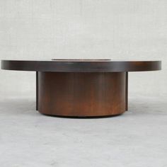 a round wooden table sitting on top of a cement floor next to a white wall